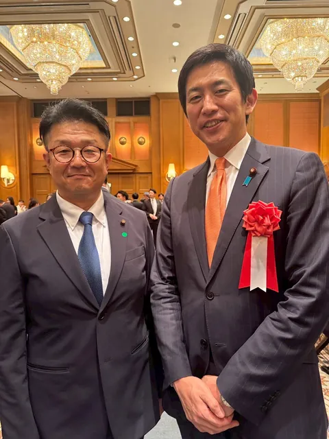 会合の会場で、スーツ姿の2人が並んだ記念写真