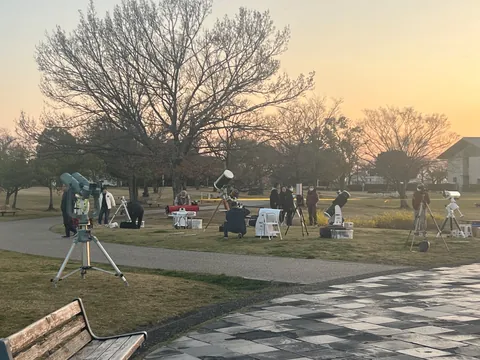 夕暮れの公園で、複数の望遠鏡を設置している様子